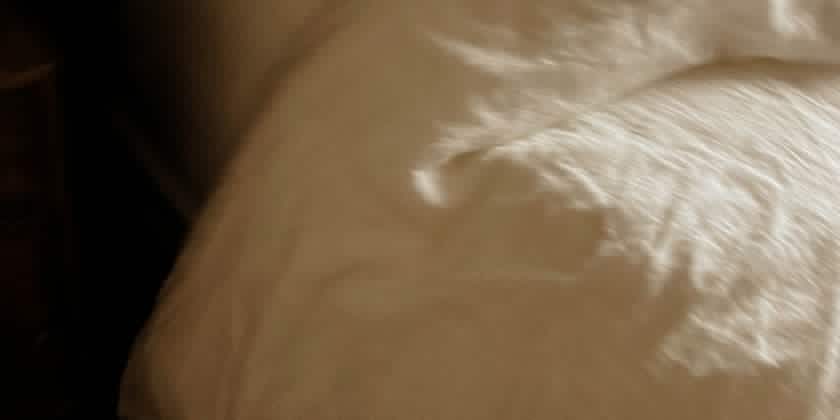 a bed with a plain white cover with natural dawn lighting